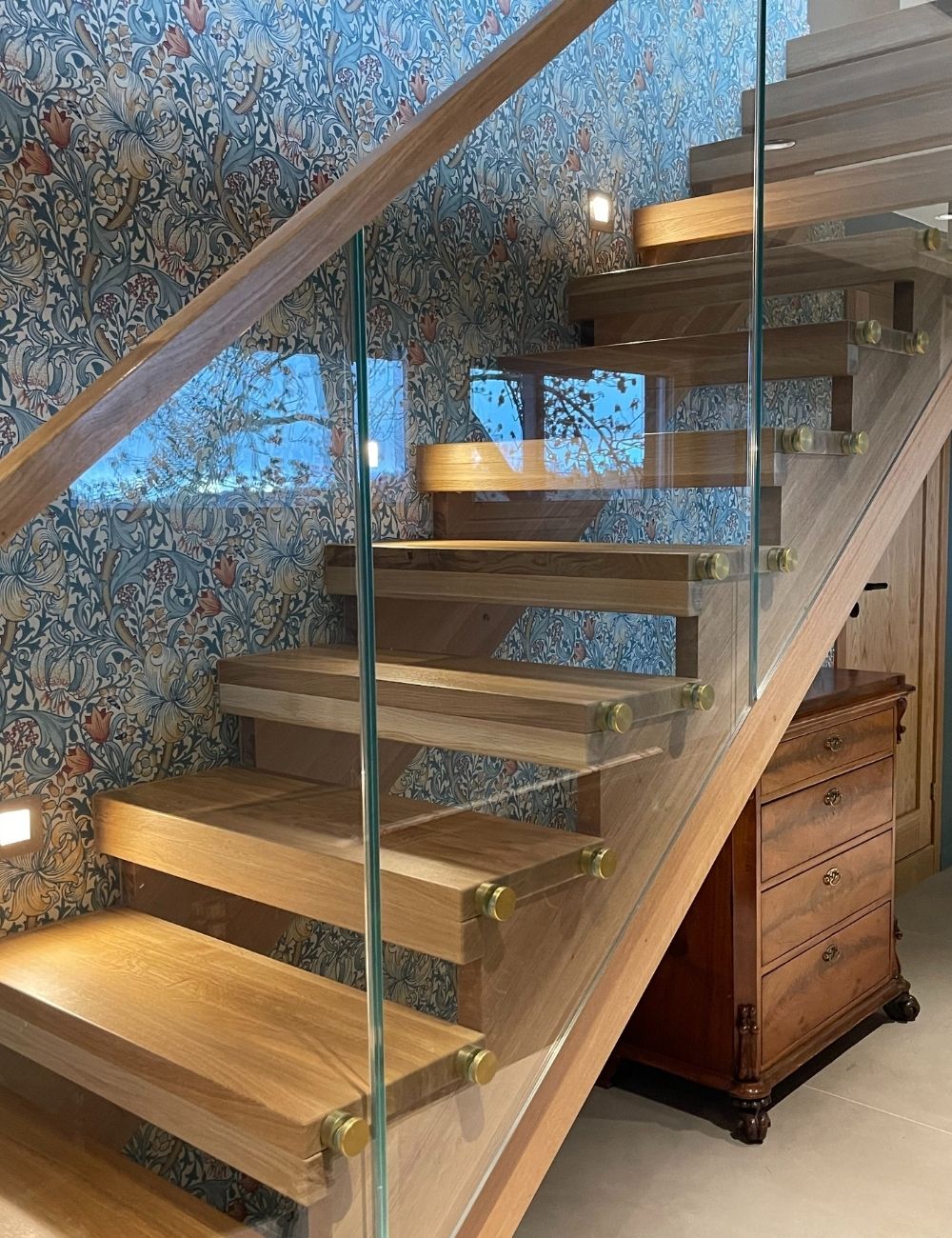 Designtrapp med alle trappens deler i beiset langstav eik, underliggende vange og boltet glassrekkverk