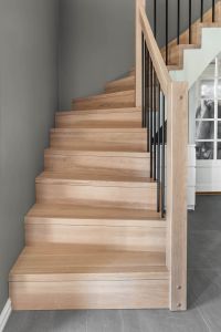 Designtrapp med underliggende vange, sortlakkerte stålspiler i rekkverk. Trinn, stusstrinn uten trappenese og stolpe i beiset langstav eik. Designtrapp med underliggende vange, sortlakkerte stålspiler i rekkverk